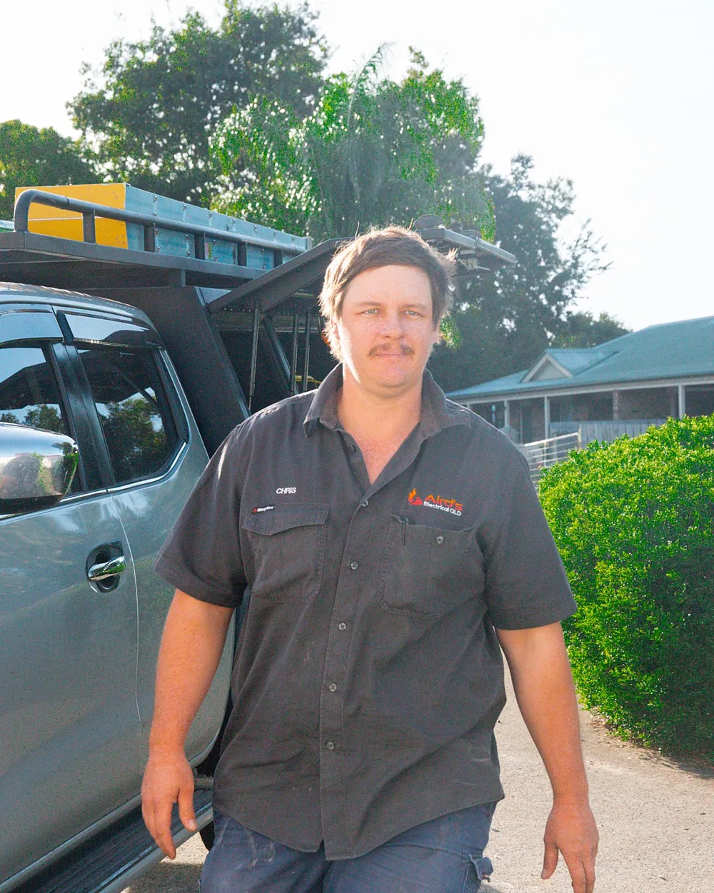 An Aird's Electrical QLD electrician in a dark grey work shirt walking from his silver ute