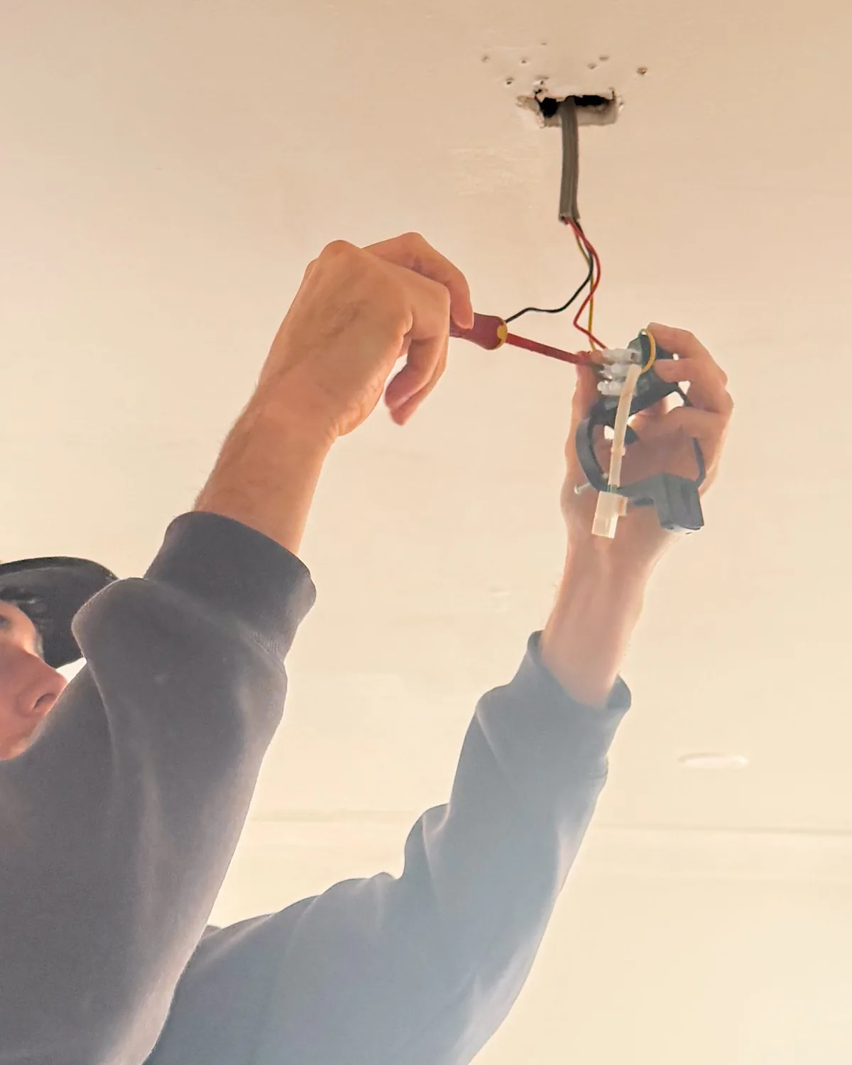 A young electrician wiring a ceiling light fitting overhead
