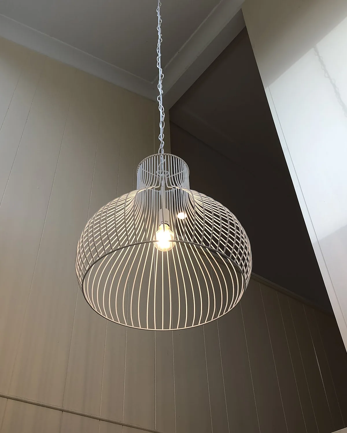 A white wire cage pendant light hanging from a raked ceiling