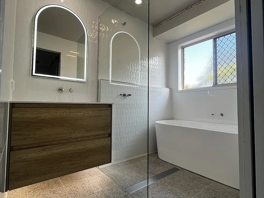 A renovated bathroom with a backlit arched mirror, downlights and an exhaust fan